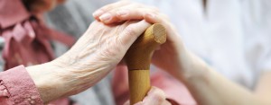 Caregiver holding an elderly person's hand on a walking stick 