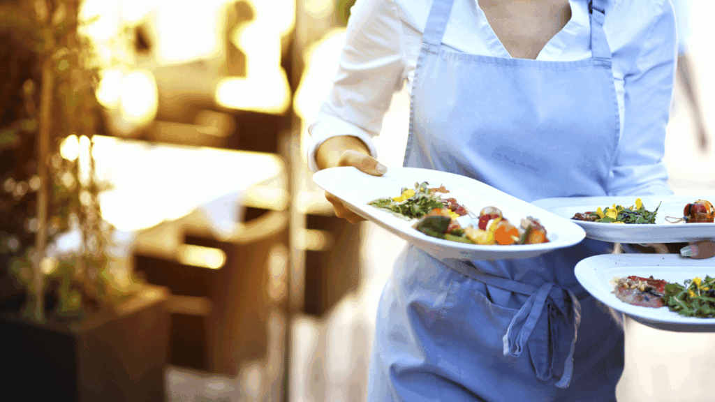 a food service worker wearing a blue apron serving three plates