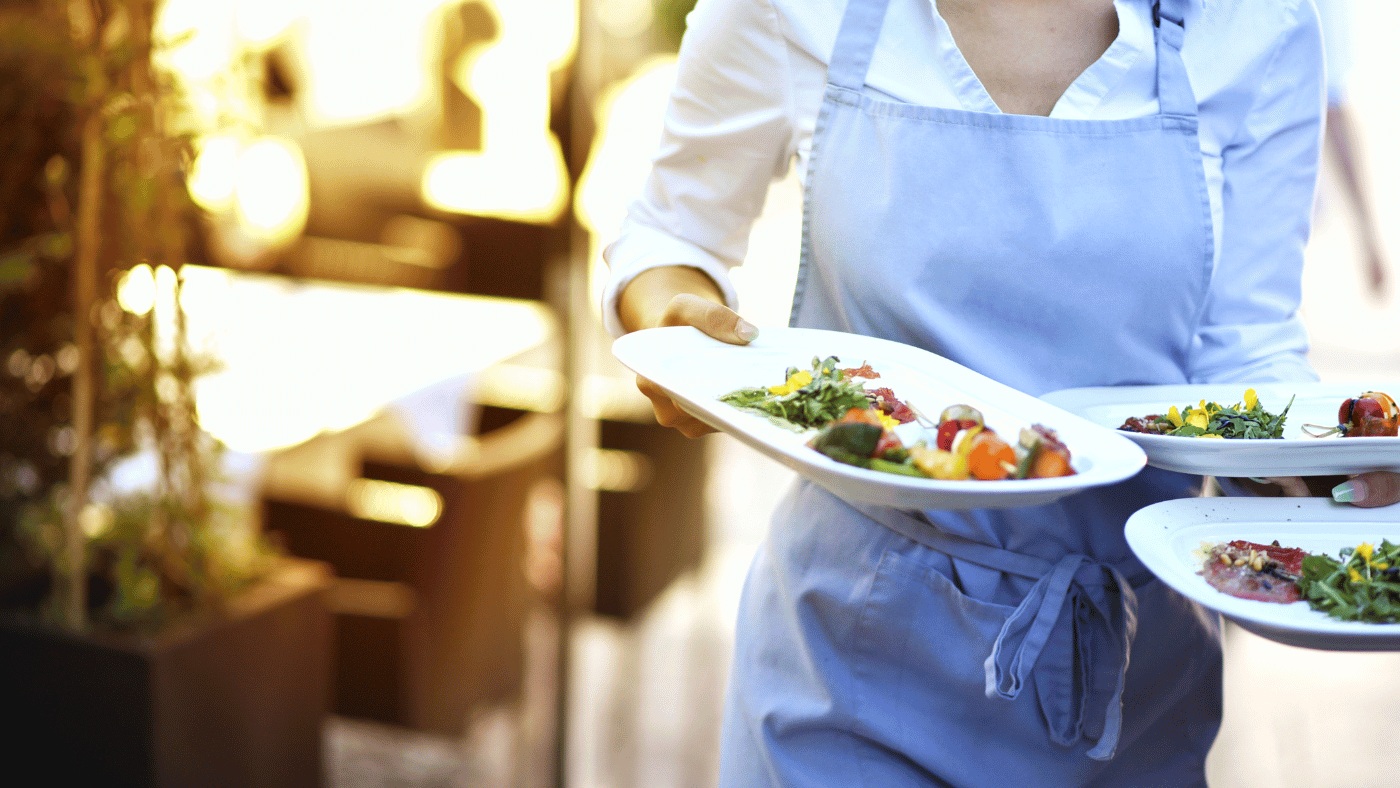 a food service worker wearing a blue apron serving three plates